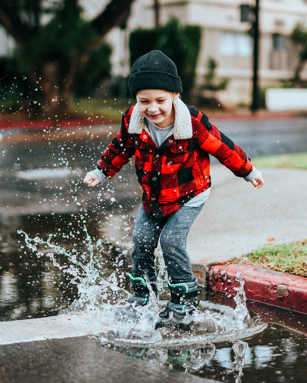 Secondhand Mode für Jungen Ein Junge trägt einen Secondhand Hemd und springt in eine Pfütze