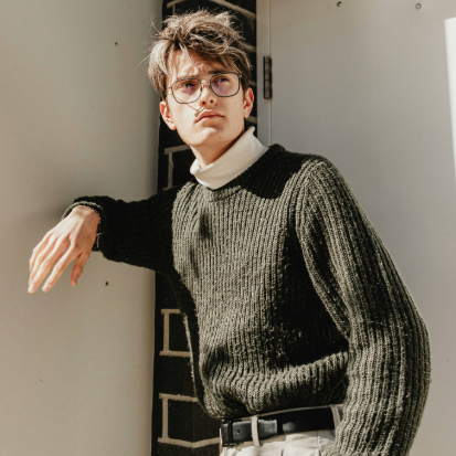 Secondhand Pullover Mann steht an einer Wand und trägt einen grünen Pullover