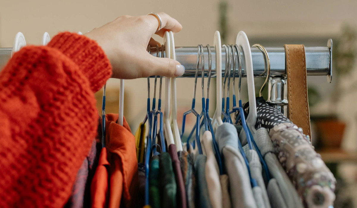 Blogartikel ReSales 7R - Nachhaltiger Modekonsum Hand greift nach Kleidungsstücken auf Kleiderstange
